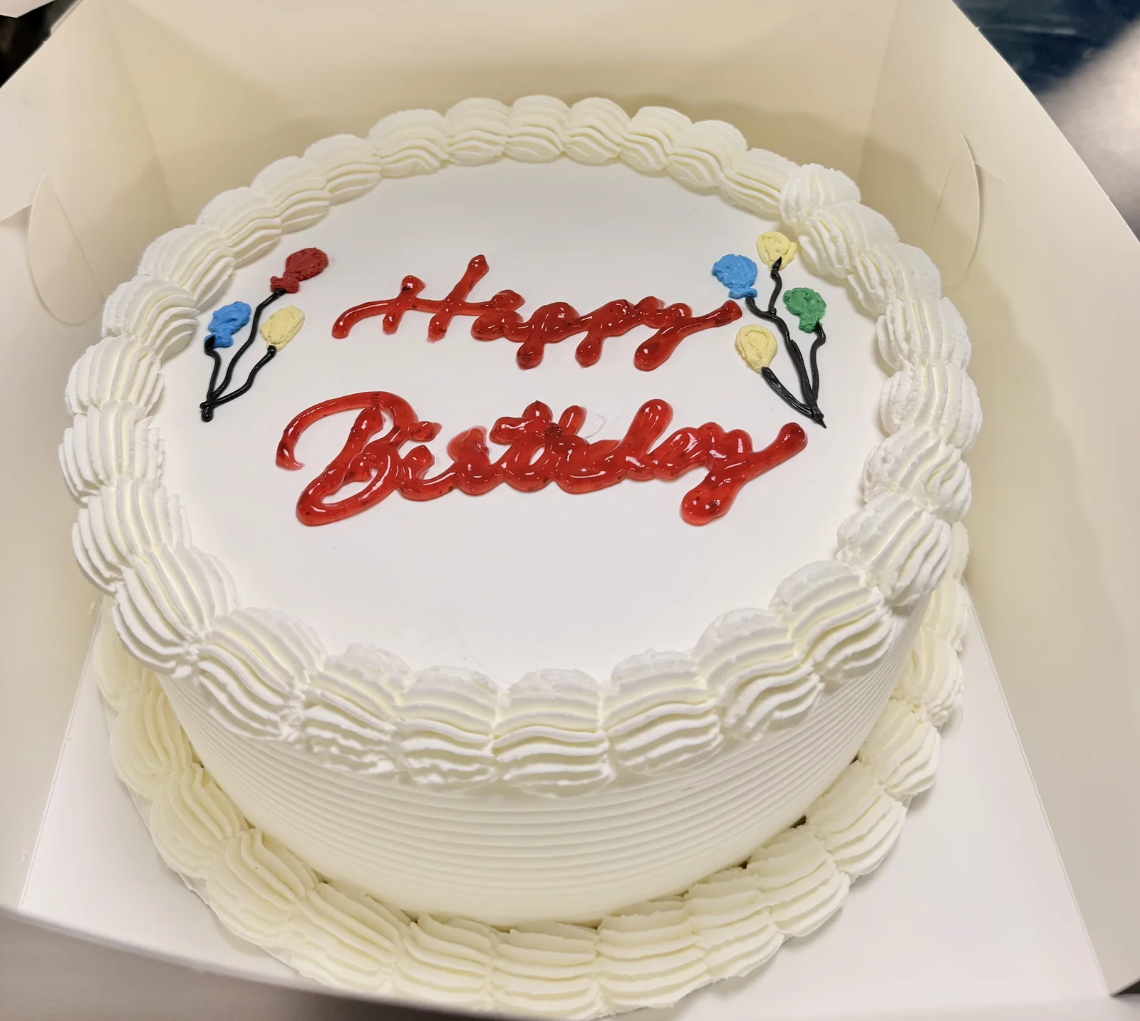 Classic white celebration cake with balloons and Happy Birthday greeting
